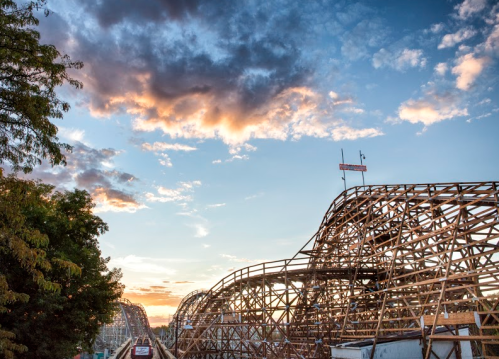 A wooden roller coaster silhouette against a colorful sunset sky with clouds.