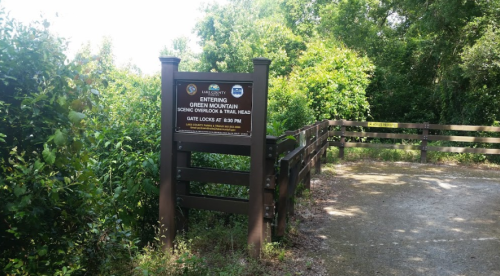 Sign marking the entrance to Green Mountain Scenic Overlook Trail Head, surrounded by greenery. Gate locks at 6:30 PM.