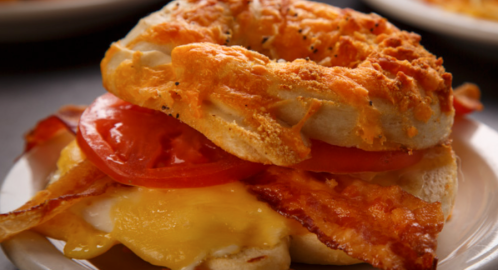 A cheesy bagel sandwich with bacon, tomato, and melted cheese on a plate.