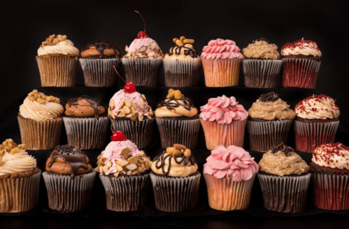 A variety of colorful cupcakes with different toppings arranged on a black background.