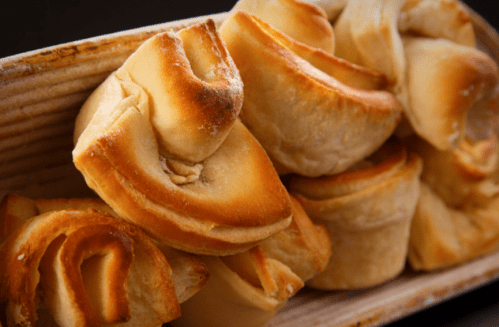 A close-up of freshly baked, golden-brown pastry rolls arranged in a wooden dish.