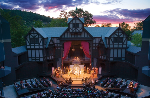A vibrant outdoor theater performance at sunset, with actors in period costumes and an audience enjoying the show.