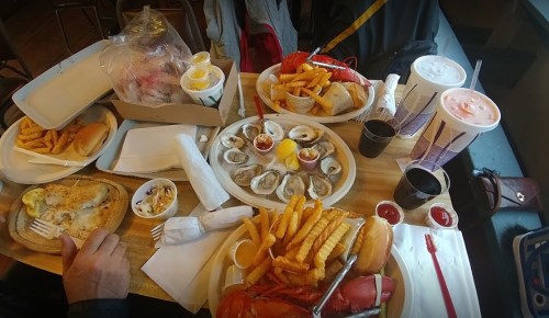 A table filled with seafood, fries, hot dogs, oysters, and drinks, showcasing a variety of dishes and condiments.
