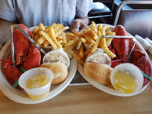 Two plates of seafood featuring lobsters, crinkle-cut fries, coleslaw, and rolls, served with lemon butter.