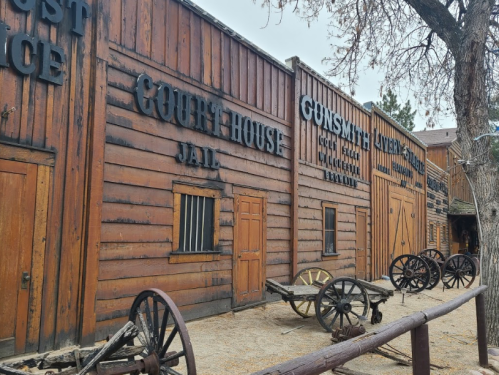 Old Western-style buildings with wooden exteriors, including a courthouse, jail, and gunsmith, alongside wagon wheels.