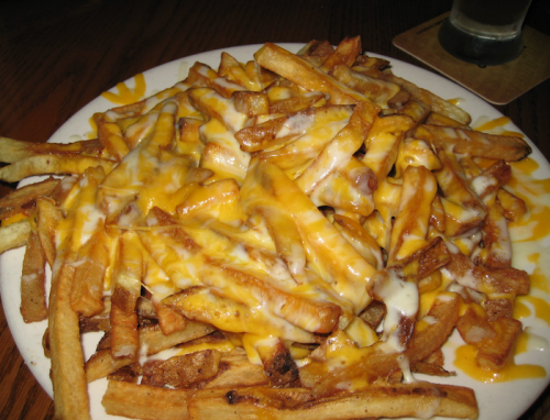 A plate of golden French fries topped with melted cheese and a drizzle of sauce.