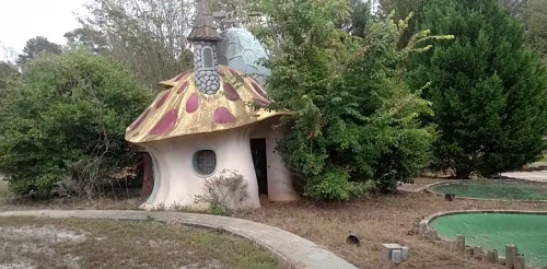 Whimsical mushroom-shaped house surrounded by overgrown greenery and a winding path.