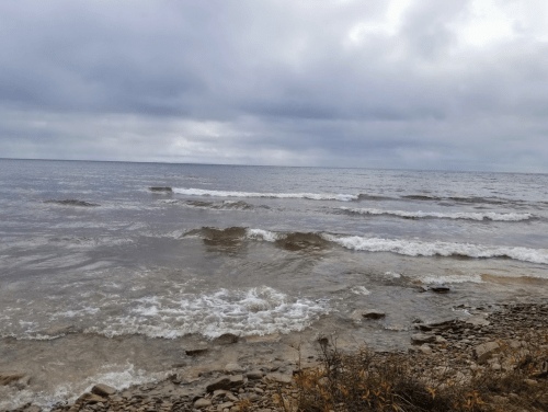 Waves gently lap at a rocky shoreline under a cloudy sky, creating a serene coastal scene.