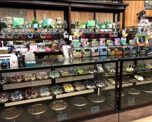 A colorful candy shop display with jars of sweets, chocolates, and treats arranged on shelves and glass cases.