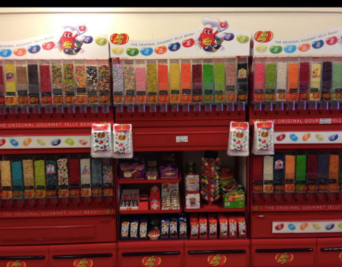 A colorful display of jelly bean dispensers and candy boxes in a store, featuring various flavors and toppings.