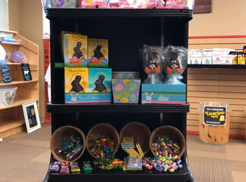 A display shelf filled with various candies, chocolate bunnies, and colorful Easter treats in baskets.
