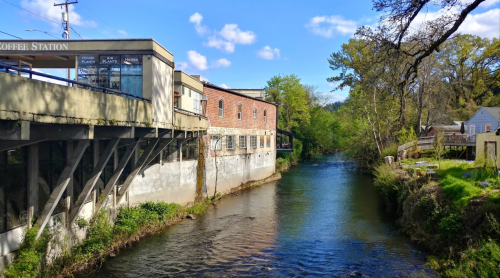A scenic view of a river beside a building with a coffee shop, surrounded by greenery and blue skies.
