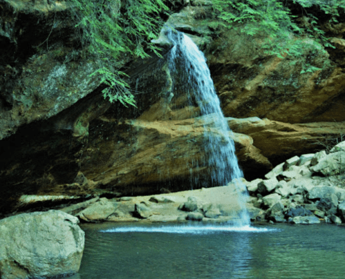 A serene waterfall cascading into a calm pool, surrounded by lush greenery and rocky terrain.