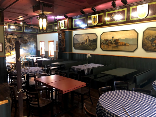 Cozy restaurant interior with checkered tablecloths, wooden chairs, and framed artwork on the walls.