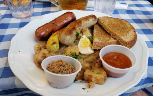 A plate with sausages, bread, mustard, and a side of sauerkraut, garnished with parsley.