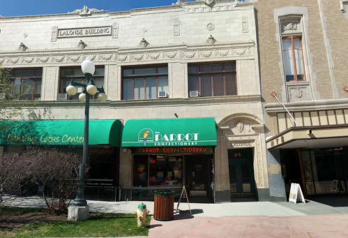 A storefront of Parrot Confectionery with green awning, located in a historic building on a sunny day.