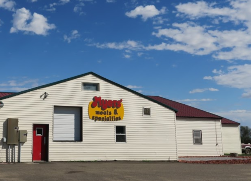 A white building with a red roof and sign reading "Myers Meats & Specialties" against a blue sky with clouds.