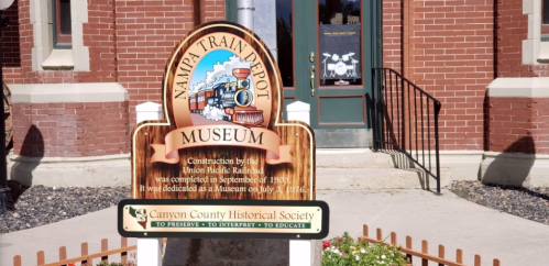 Sign for the Nampa Train Depot Museum, detailing its construction and dedication date, with a historical society logo below.