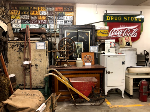 A collection of vintage items including a spinning wheel, antique furniture, and old signage in a nostalgic setting.