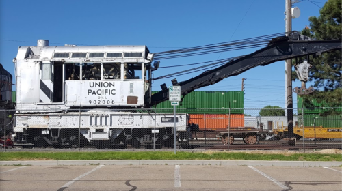 A Union Pacific crane truck parked beside a fence, with freight containers in the background under a clear blue sky.