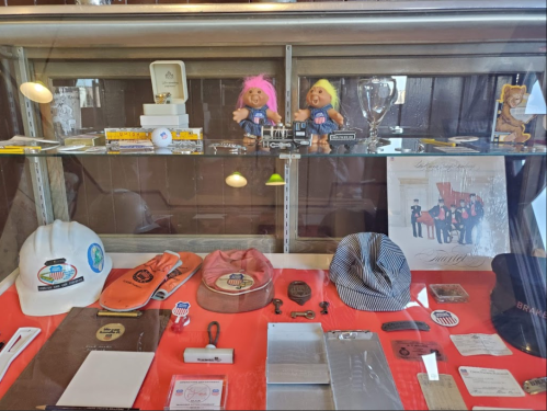 Display case featuring vintage memorabilia, including dolls, hats, and various collectibles on a red background.