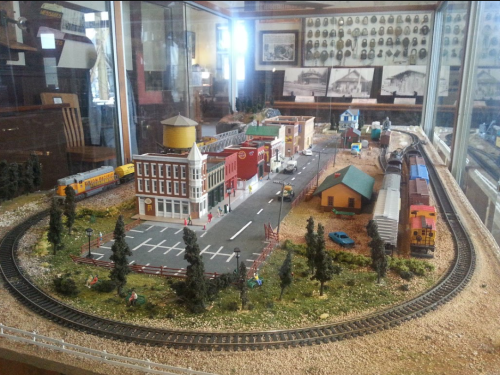 A detailed model train display featuring a town with buildings, trees, and a railway track.