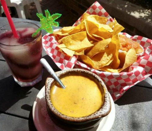 A bowl of creamy dip with a side of tortilla chips and a drink with a garnish on a table.