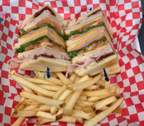 A stacked club sandwich with layers of turkey, ham, cheese, and lettuce, served with a side of French fries in a basket.