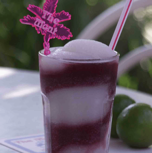 A colorful frozen drink in a glass with a pink straw and decorative stirrer, garnished with lime.
