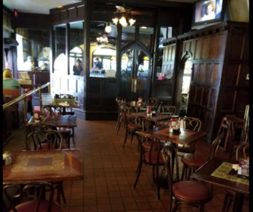 Interior of a restaurant featuring wooden tables and chairs, with a dark wood decor and a TV in the background.