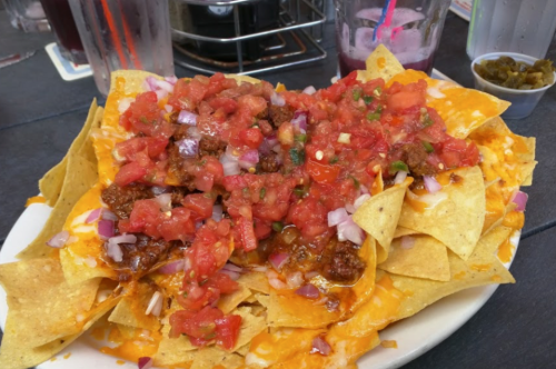 A plate of nachos topped with melted cheese, salsa, onions, and jalapeños, served in a casual dining setting.