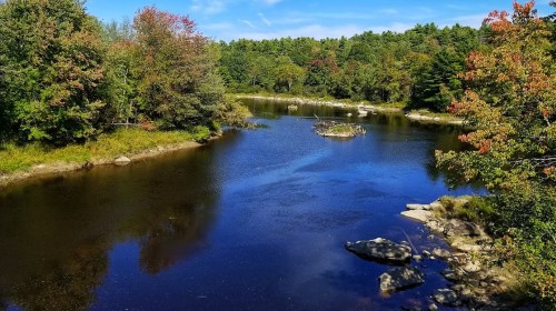 A serene river flows through a forested landscape, with colorful autumn foliage and rocky banks.