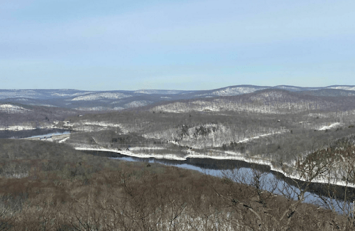 Snow-covered hills and a winding river under a clear blue sky, showcasing a serene winter landscape.