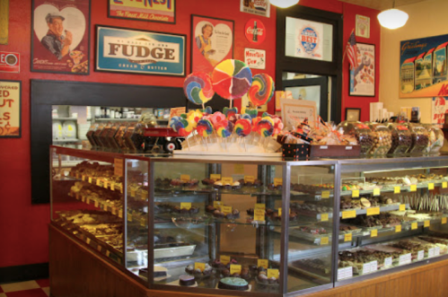 A colorful candy shop display featuring fudge, chocolates, and lollipops in a vintage-style interior.
