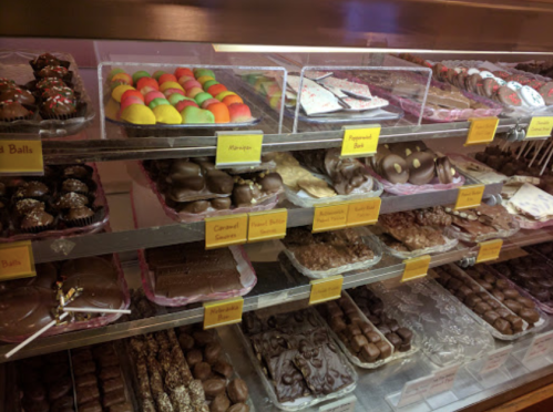 A display case filled with various chocolates and confections, labeled with names and colorful treats.