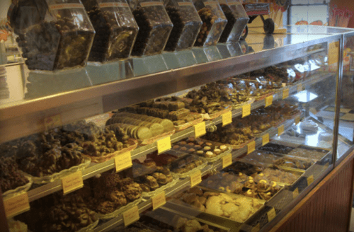 A display case filled with various chocolates and confections, labeled with yellow tags, in a colorful shop.