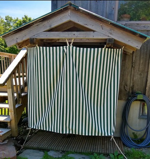 A wooden structure with a striped green and white curtain covering the entrance, next to a staircase and garden hose.