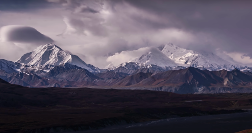 Majestic snow-capped mountains under a dramatic cloudy sky, showcasing rugged terrain and serene beauty.
