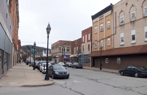 A quiet downtown street with parked cars, historic buildings, and a lamppost under a cloudy sky.