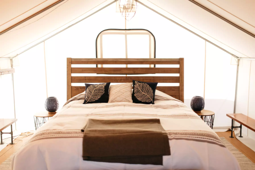Cozy tent interior featuring a wooden bed with decorative pillows, side tables, and warm lighting.
