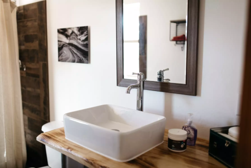 A modern bathroom featuring a white vessel sink, wooden countertop, mirror, and decorative wall art.