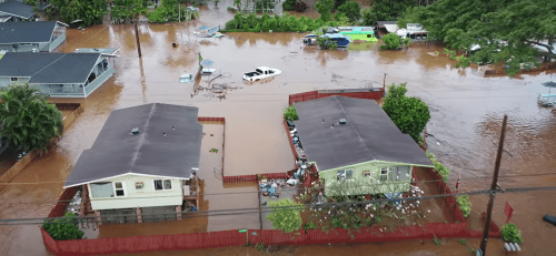 Aerial view of flooded homes and vehicles surrounded by rising water in a residential area.