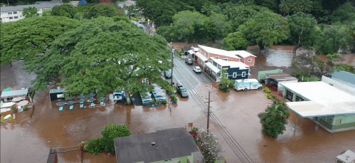Aerial view of a flooded street with submerged buildings and trees, showcasing significant water damage in the area.