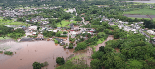 Aerial view of a flooded area with submerged homes and roads surrounded by lush greenery.