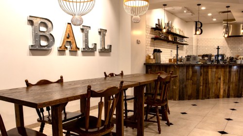 A cozy café interior featuring a wooden table, chairs, and a wall with the word "BALL" in decorative letters.