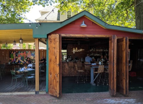 A cozy restaurant with a wooden bar, outdoor seating, and colorful artwork on the walls.