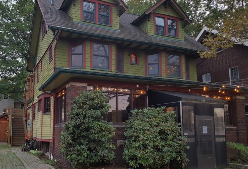 A colorful three-story house with green and red accents, surrounded by greenery and string lights.