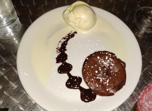 A plate with a chocolate dessert, drizzled with sauce, and a scoop of vanilla ice cream on the side.