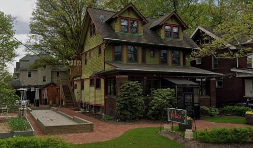 A colorful, multi-story house with green siding and red trim, surrounded by trees and a garden area.