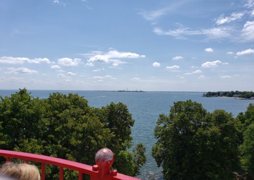 A scenic view of a lake with trees in the foreground and a clear blue sky with clouds in the background.